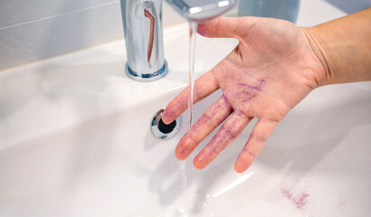 Close up of unrecognizable woman washing purple glitter of her hand into basin at bathroom and...