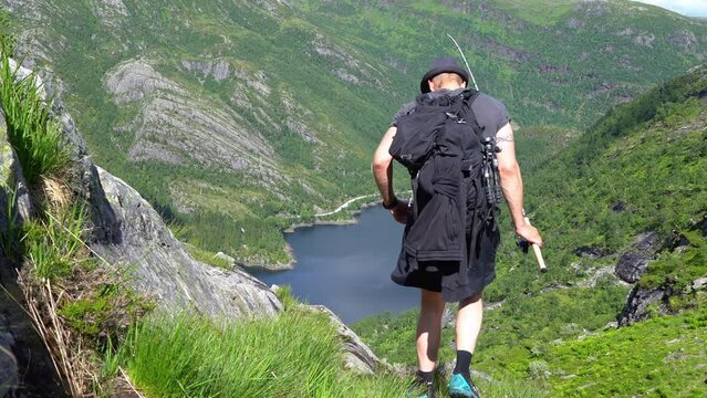 Man complete mountain fishing trip and proceeds downhill towards Bergsdalen Norway while holding fishing rod in hs hand