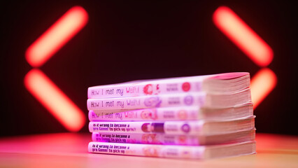 Stacking Japanese manga comics on pile studio shot with neon lights in background