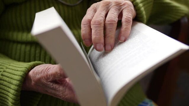 Elderly individual using their hands to turn the pages of a book