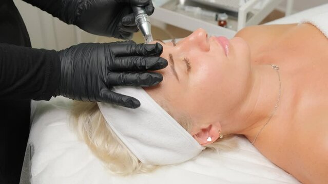 Close-up portrait of a beautiful aged woman during microneedling with dermapen from a beautician.