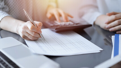 Woman accountant using a calculator and laptop computer while counting taxes for a client. Business...