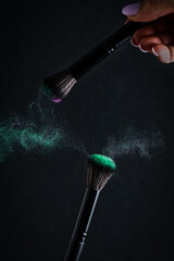 Make-up brush with emerald powder explosion on black background.