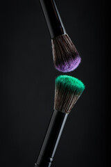 Make-up brushes with emerald  and lilac powder on black background.