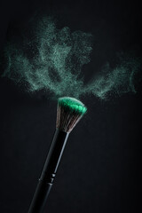 Make-up brush with emerald powder explosion on black background.