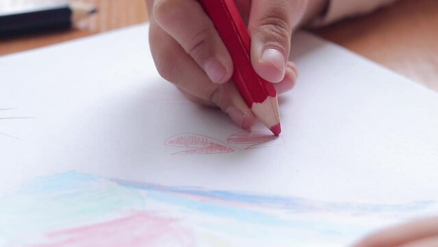 A child draws with colored pencils in an album. Children's creativity, learning in kindergarten, school or at home. Child's hand with a pencil close-up, selective focus. Girl draws a picture