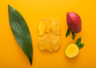 Sweet dried large mango slices on yellow background with raw fruit and leaf.