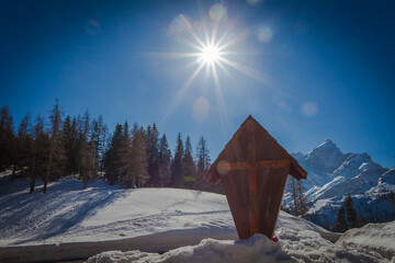 Fototapeta premium Wooden crucifix at the Staulanza Dolomite pass. Sun over Mount Civetta landscape in the background. Val di Zoldo, Belluno, Italy