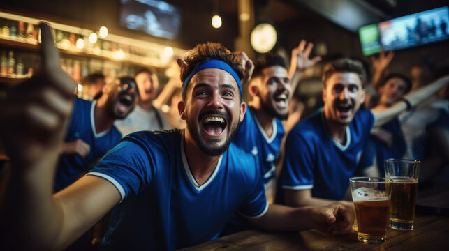 Fototapeta Group of friends in blue shirts with beer glasses looking happy at soccer games in a bar.