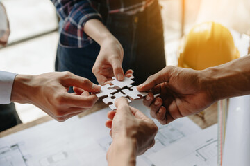 Obraz premium Construction team shake hands greeting start new project plan behind yellow helmet on desk center to consults about their building project. hand connecting jigsaw puzzle