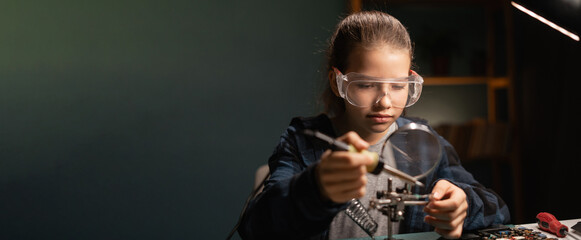 Cute girl in safety glasses, learning how to solder microprocessor cables and printed circuits uses...