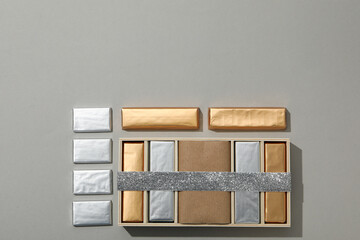 Chocolates in foil and in box with ribbon on gray background, space for text