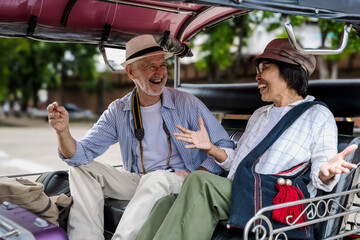 Cheerful senior tourist couples sitting on tuktuk during summer vacation in Thailand