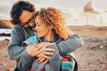 Love and travel people together. One man hug woman from behind in romantic outdoor leisure activity together. Desert scenic landscape in background with windmills and sunset time. Adventure traveler - obrazy, fototapety, plakaty