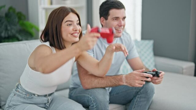 Beautiful couple playing video game sitting on sofa celebrating at home
