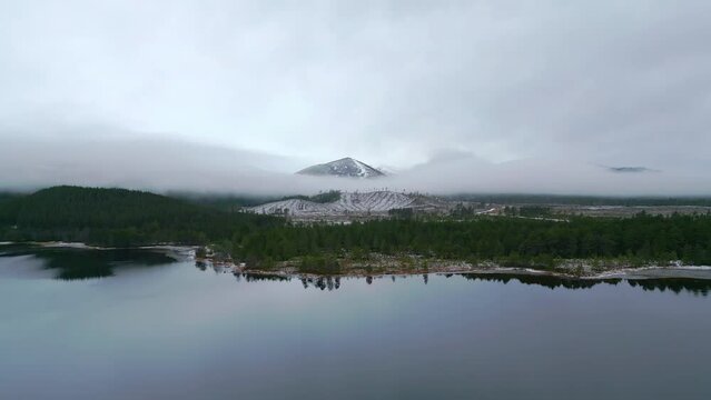 Heading across flat lake over forest towards a mist shrouded snow capped mountain
