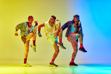 Three young men in colorful sportswear and accessories training aerobics against gradient yellow blue background in neon light. Concept of sportive and active lifestyle, humor, retro style. Ad
