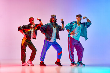 Strength. Three young men, friends wearing colorful old style sportswear, showing muscles against gradient pink blue background in neon light. Concept of sportive and active lifestyle, retro. Ad