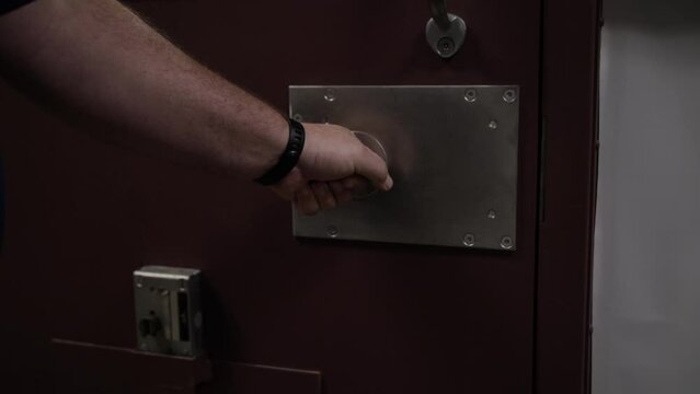 Prison guard shuts and locks prisoner inside prison door in cinematic slow motion.