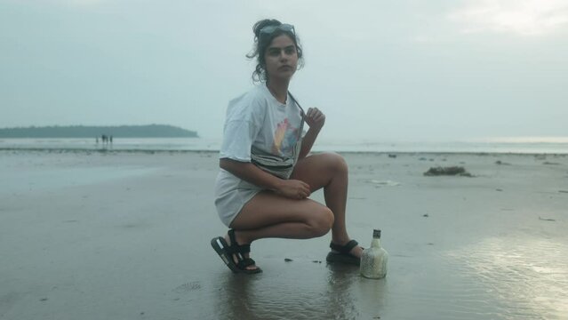 Young Woman Exploring the Beach next to a Sunken Bottle while adjusting her Pack