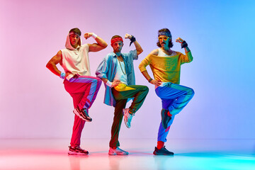 Men in vintage, colorful sportswear posing, doing aerobics exercises against against gradient pink...