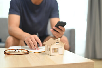 A detached house on table with man using calculator for planning and calculating money for buy...