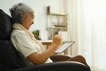 Beautiful middle age woman using digital tablet on comfortable armchair. People and technology concept