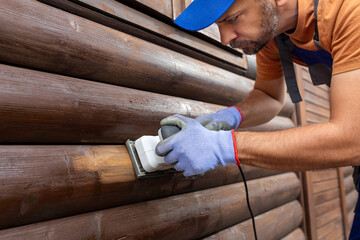 Worker sanding a wooden window shutters on house exterior.
