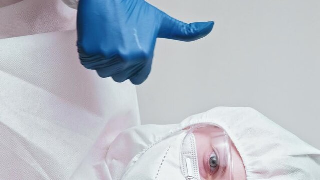 Vertical video. Medical virologist. Covid-19 protective equipment. Approval gesture. Lab nurse woman in coverall suit thumb up hand sign isolated on grey background.