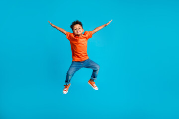 Fototapeta na wymiar Full body cadre of jumping energetic latin small kindergarten age boy hands up positive star symbol hands isolated on blue color background
