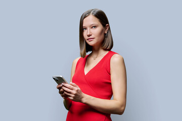 Naklejka premium Young woman holding smartphone, looking at camera on gray background