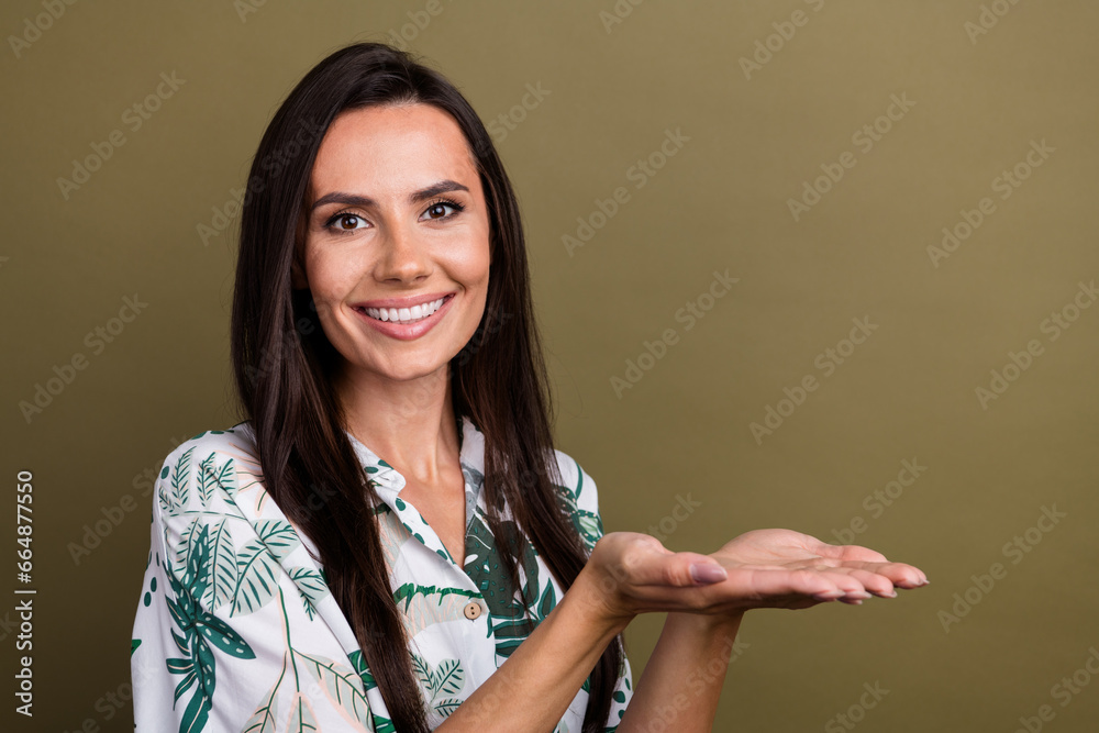 Sticker Photo of toothy beaming lovely girl dressed flower print blouse palms demonstrate product empty space isolated on brown color background