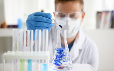 Fototapeta premium A male chemist holds test tube of glass in his hand overflows a liquid solution of potassium permanganate. Conducts an analysis of water samples versions of reagents using chemical manufacturing.