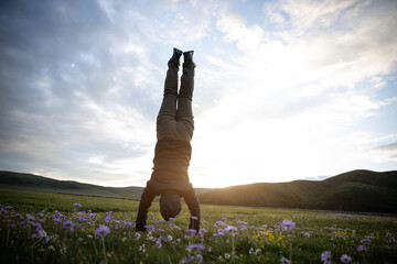 Woman hiker doing a handstand on high altitude mountain meadow