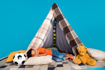 Photo of little sweet boy sleeping in diy tepee isolated over blue color background - obrazy, fototapety, plakaty