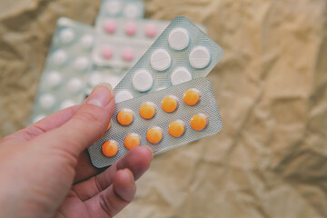 Woman's hand with multicolored pills in blisters against beige craft paper