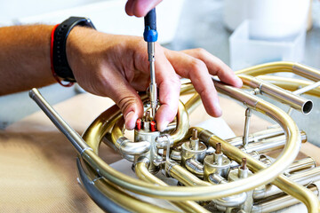 repairman assembling a cylinder of a French horn on the table in repair shop