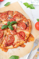 Pizza margherita with basil on a white background. Pizza with cheese and tomatoes cut into pieces. Homemade baking.