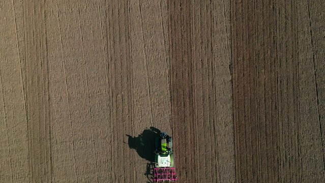 Luftaufnahme eines Traktors mit Pflug, der den Boden auf einem braunen Feld pfl&uuml;gt und durch das Sichtfeld f&auml;hrt