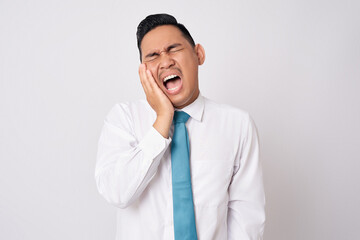 Unhealthy young Asian businessman wearing formal shirt and tie feeling dental problem and pressing sore cheek, suffering acute toothache isolated on white background - obrazy, fototapety, plakaty