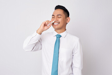 Young Asian businessman wearing a formal shirt and tie shows a relieved expression when using nasal...