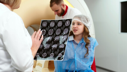 In a modern clinic, a female radiologist explains the good results of a CT scan of a young patient,...