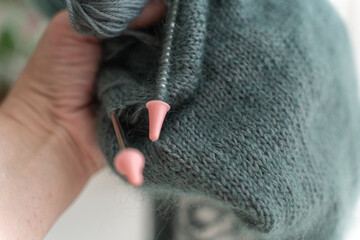 Hands of young woman holding the knit needles with the hand-made work on them. Eco frendly craft....