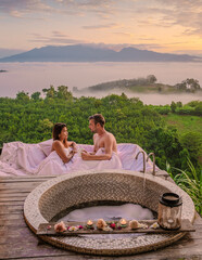a couple of men and women in a bathtub looking out over the mountains of Northern Thailand during vacation. Outdoor bathroom, and bathtub during sunrise at the mountains of Nan with mist and fog