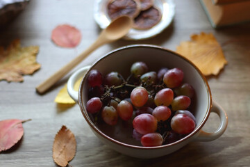 Cup of tea or coffee, plate with desserts, dried oranges, bowl of grapes, scented candles, vintage books, pumpkins and autumn leaves on the table. Autumnal hygge. Selective focus.