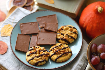 Cup of tea or coffee, plate with desserts, dried oranges, bowl of grapes, scented candles, vintage books, pumpkins and autumn leaves on the table. Autumnal hygge. Selective focus.