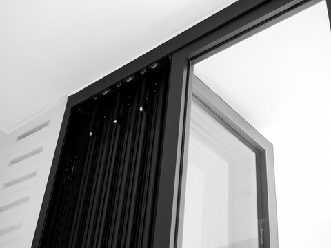 Close-up door hinges on the black aluminum folding doors with glass on white building background, indoor and outdoor partition, interior doorway decoration.