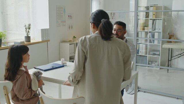 Latin mom escorting her little daughter while visiting Middle Eastern male pediatrician in modern office