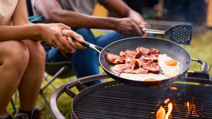 Close Up Of Couple Camping In Countryside With RV Cooking Bacon And Eggs For Breakfast On Fire