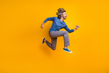 Fototapeta na wymiar Full length photo of cheerful excited man wear blue sweater jumping high running fast isolated yellow color background